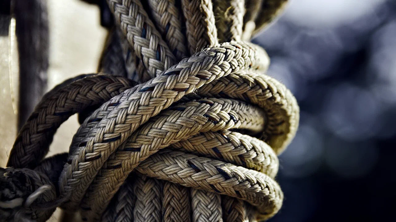 A close-up of a thick brown rope knotted against a dark background